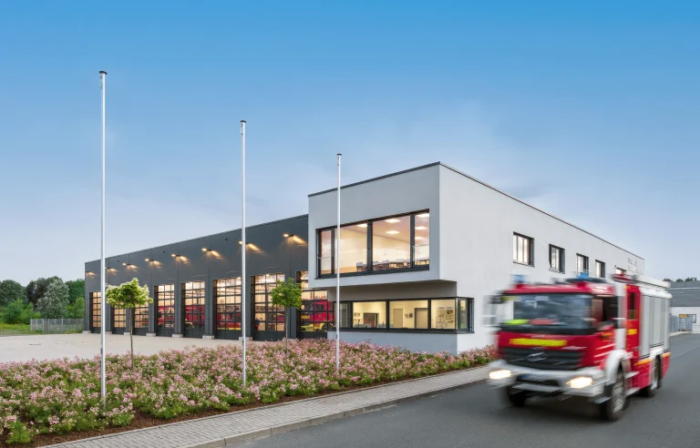 Modernes Feuerwehrgebäude mit ausrückendem Feuerwehrfahrzeug bei Tageslicht