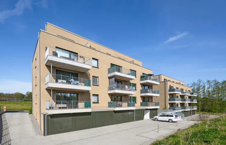 Modernes Mehrfamilienhaus mit Balkonen und Garagen unter blauem Himmel.