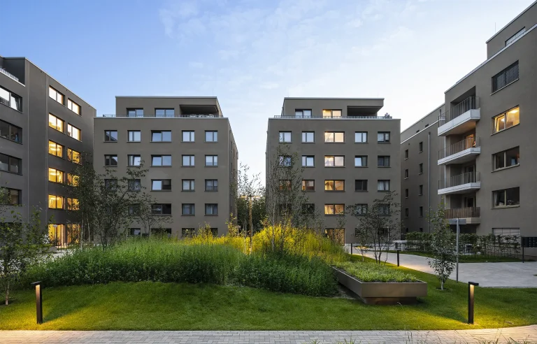 Moderne Wohngebäude mit Grünfläche im Innenhof bei Sonnenuntergang.